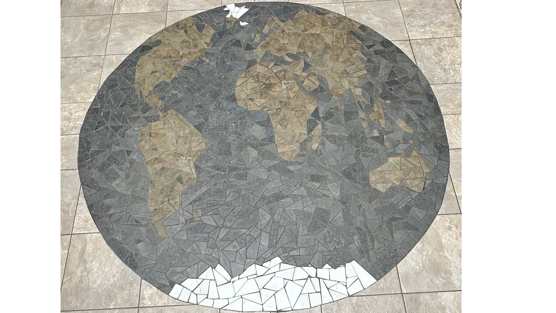 Circular stone floor mosaic depicting a world map with tan continents and grey oceans.