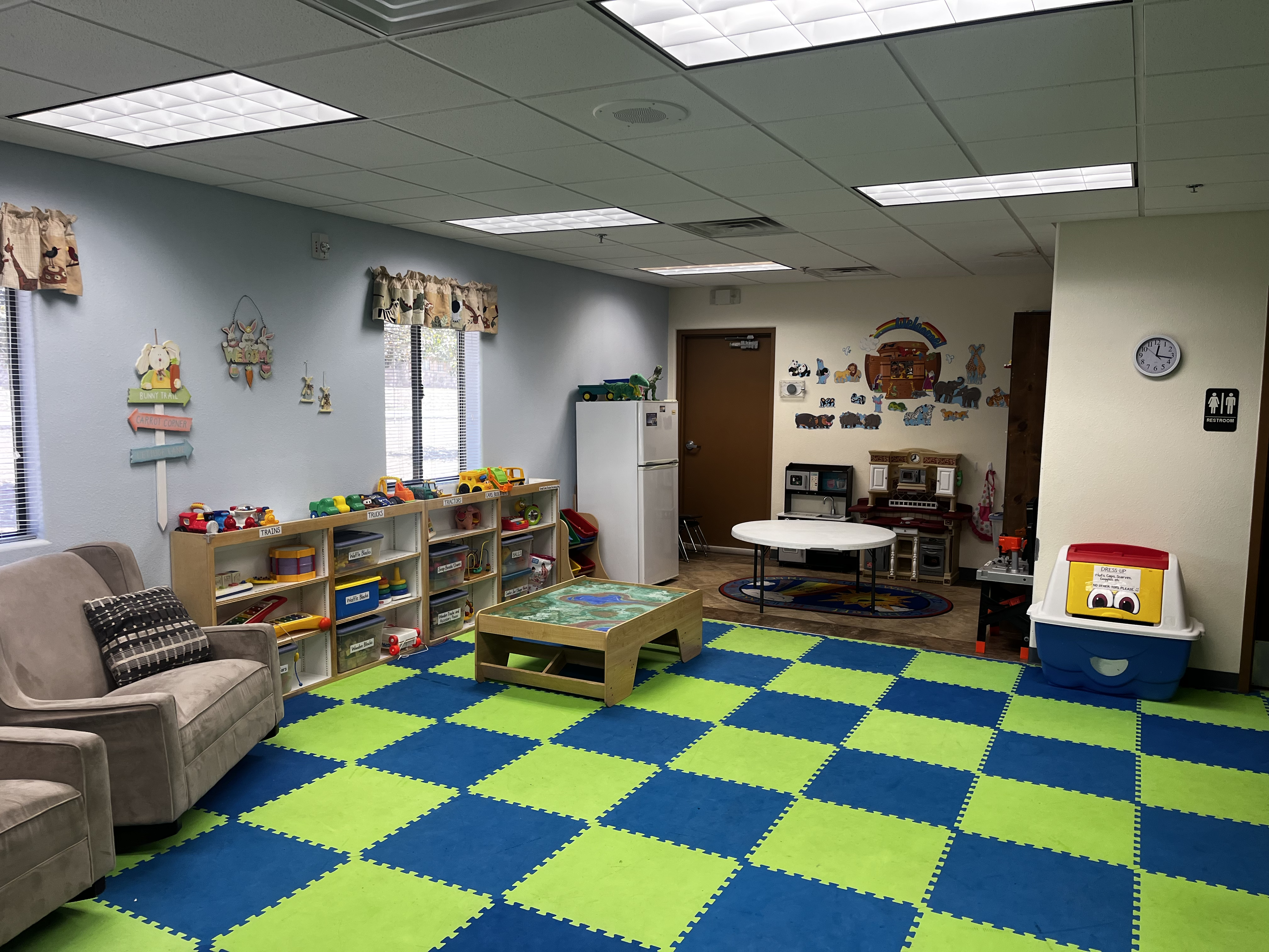 Colorful playroom with blue and green checkered mats, toy shelves, and a play kitchen area.