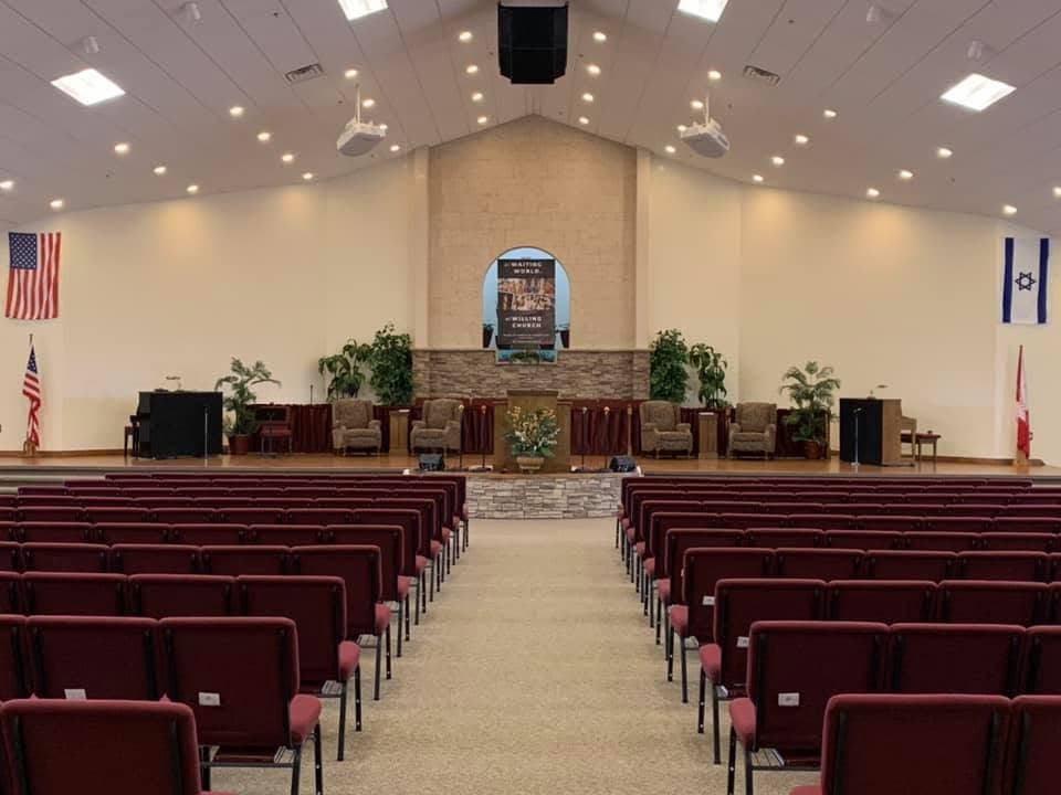 Spacious church sanctuary with rows of red chairs facing a stage and a central podium.